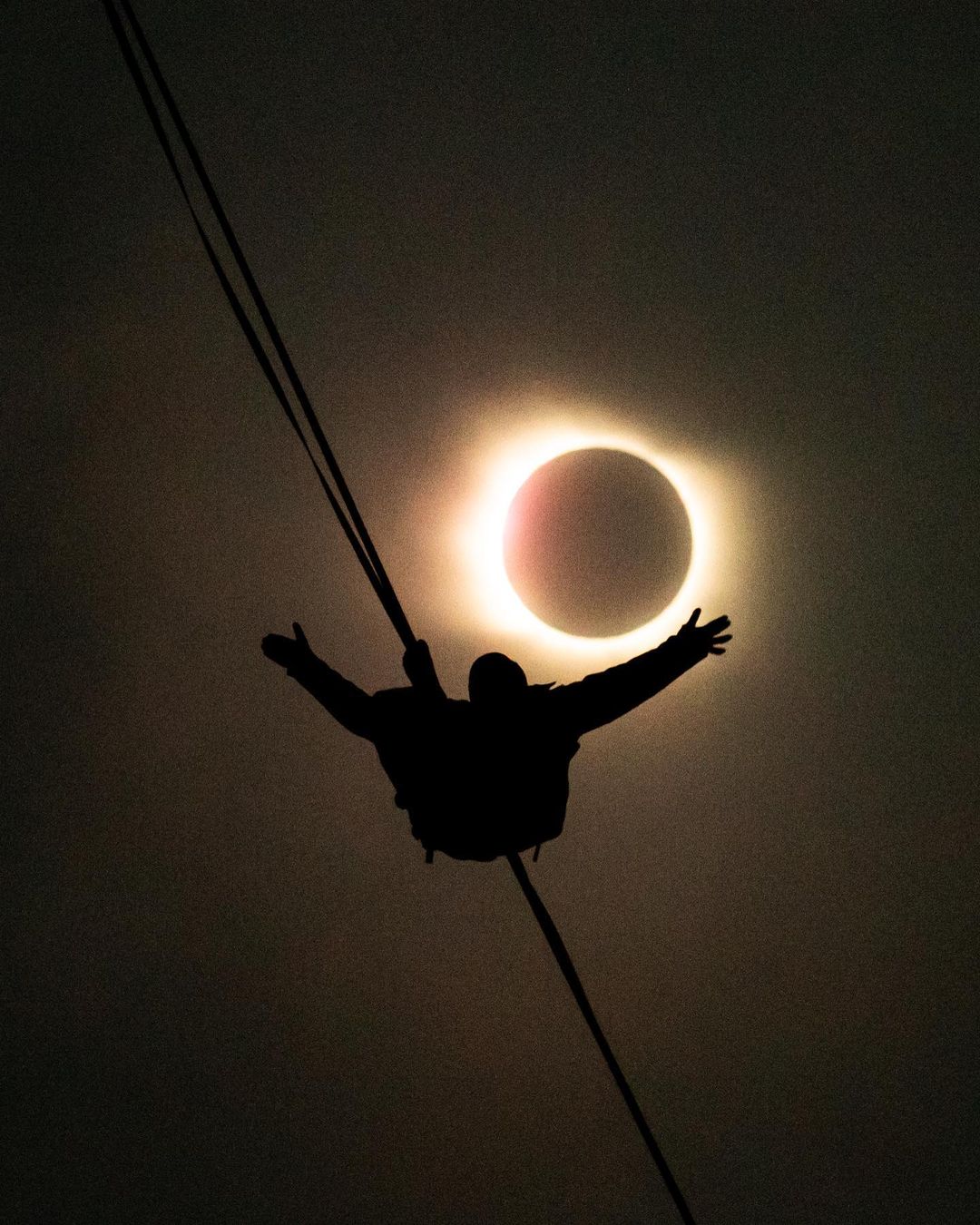 Imagen de un hombre caminando por una cuerda en medio del eclipse 2020